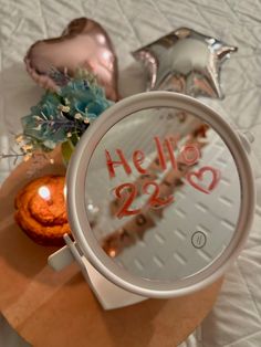 a round mirror with the word hello 223 on it next to some balloons and flowers