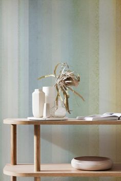 a table with vases and books on it in front of a striped wallpaper