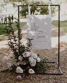 a sign that is sitting on top of a stand with flowers in front of it