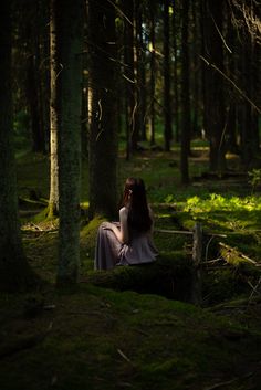 a woman sitting in the middle of a forest