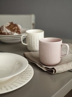 two coffee mugs sitting next to each other on top of a table with plates