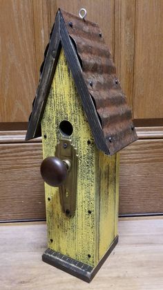 a yellow birdhouse with a brown roof and door knobs on the side of it