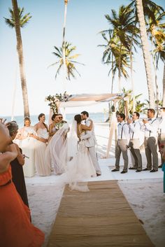 a couple getting married on the beach in front of their wedding party and guests watching