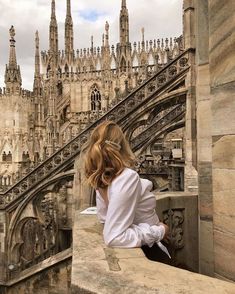 a woman sitting on the edge of a stone wall looking down at an old building