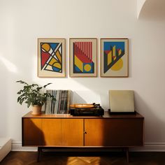 three paintings hang on the wall next to a record player and a potted plant