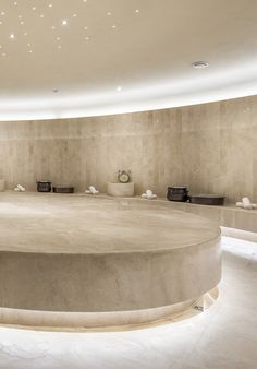 a large circular room with white marble walls and flooring is lit by recessed lights