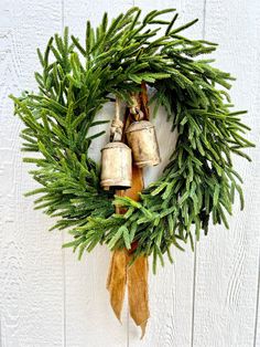 a wreath with two bells hanging from it's side on a white wooden wall