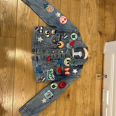 a child's jean jacket with patches and buttons on the back, sitting on top of a wooden floor