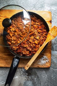 a skillet filled with food sitting on top of a wooden cutting board next to a spatula