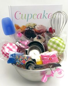 a metal bowl filled with cupcakes next to a cookbook and whisk