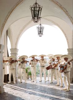 a group of men in white suits and hats playing instruments under an archway with a light hanging from the ceiling