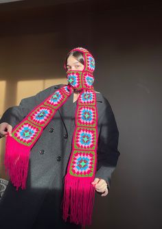 a woman wearing a scarf and jacket with a hat on her head standing in front of a wall