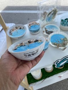 a hand holding a bowl filled with blue liquid next to other dishes on a table