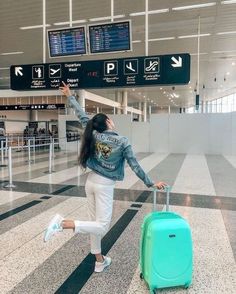 a woman is standing with her luggage at the airport and reaching up to catch an airplane