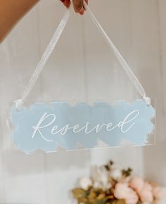 a person holding a sign that says reserved hanging from a string with flowers in the background