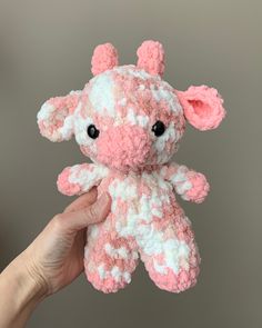 a pink and white stuffed animal being held up by someone's hand with black eyes