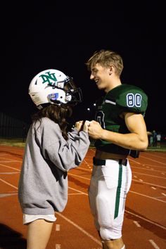 a couple of people standing on top of a field with a football uniform and helmet