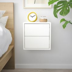 a white nightstand with a clock on it next to a plant