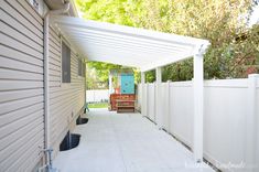 a white covered patio area with a blue door and wooden bench on the far side