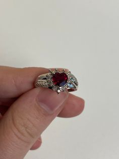 a hand holding a ring with a red stone in the middle and white diamonds around it