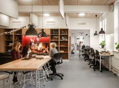 people sitting at desks in an office with open shelving and hanging lights above them