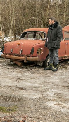 a man standing next to an old rusted out car