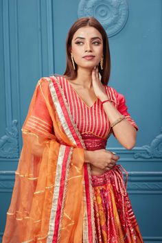 Red embroidered bandhej lehenga with a contrasting orange dupatta online in the USA. Featuring embroidered blouse with 3/4th sleeves blouse The Lehenga comes with a look royal at weddings and festive occasions in exquisite designer sarees, gowns, lehngas, Anarkali, and suits Pure Elegance Indian saree stores in the USA. Red Bandhani Print Lehenga For Traditional Ceremonies, Orange Bollywood Choli With Bandhani Print, Orange Bandhani Print Traditional Wear For Festivals, Festive Orange Choli With Bandhani Print, Orange Sharara For Traditional Ceremonies And Festivals, Fitted Orange Bandhani Traditional Wear, Orange Festive Sharara For Traditional Ceremonies, Orange Lehenga With Cutdana For Traditional Ceremonies, Orange Sharara With Dupatta For Traditional Ceremonies