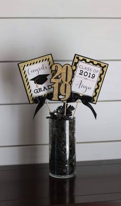 a graduation centerpiece in a clear vase with black and gold decorations on the top