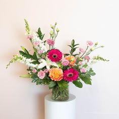 a vase filled with lots of colorful flowers on top of a white table next to a wall