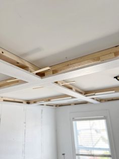 an unfinished room with white walls and wood beams on the ceiling, in front of a window