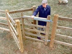 an old man standing in front of a wooden fence with sheep behind it and looking over the gate