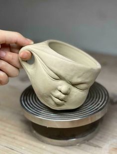 a person is holding a clay face on top of a stand that holds a vase