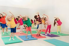 a group of children standing on yoga mats in front of a wall with their arms up