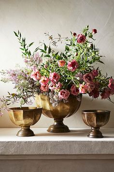 three vases with flowers in them sitting on a table next to each other,