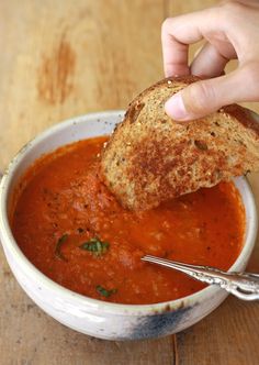 a person dipping bread into a bowl of tomato soup