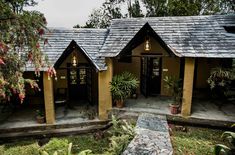 a small house with two porches in the front and one on the side, surrounded by greenery