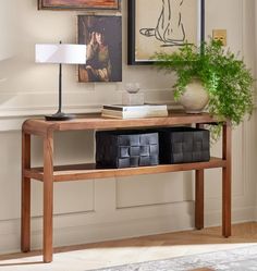 a wooden table with two baskets on it next to a lamp and pictures hanging on the wall