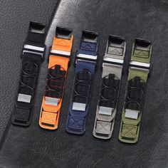 four different colored straps sitting on top of a black leather seat belt with metal buckles