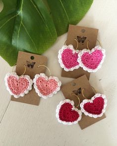 four crocheted heart shaped earrings on top of a table next to a plant