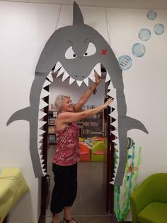 an older woman standing in front of a giant shark cutout with her hand out