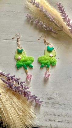 two green and pink earrings sitting on top of a wooden table next to lavender flowers