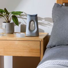 a wooden table topped with two cups and a vase filled with plants next to a bed