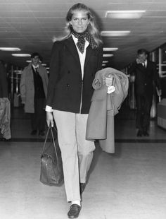 a black and white photo of a woman carrying luggage in an airport terminal with other people behind her