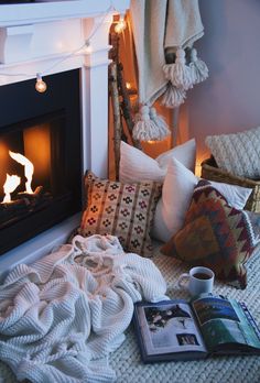 there is a book and some pillows on the bed next to a fireplace with a lit candle