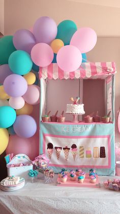 an ice cream stand with balloons and cupcakes on the table in front of it