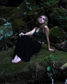 a woman sitting on top of a moss covered rock