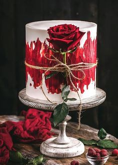 a white and red cake with roses on the top is sitting on a wooden table