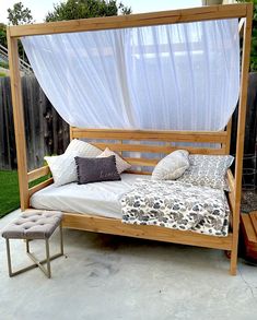 a bed with a canopy and pillows on it in a backyard next to a fence