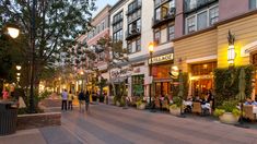 people are sitting at tables on the side walk in front of shops and restaurants with tall buildings behind them