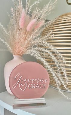 a pink vase sitting on top of a white table next to a basket filled with feathers